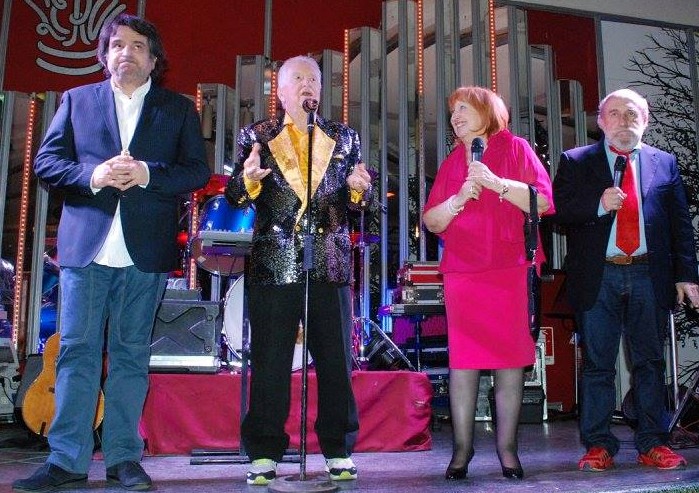 Gianfranco D'angelo con giacca a paillette e risvolto giallo, pantalone nero, davanti al microfono su un palco insieme a Margherita Fumero, vestita con tailleur rosa, Sergio Vastano, con completo nero e Enroco Beruschi con completo scuro, camicia bianca e cravatta rossa