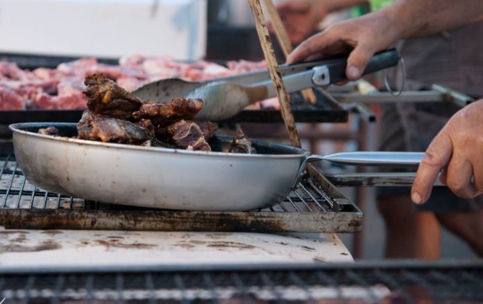 nella foto si vedono le mani di un cuoco mentre cucina dei pezzi di carne in un apadella di ghisa sopra una griglia