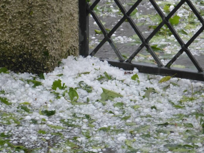 Temporali in arrivo nella foto un cancello con per terra dei mucchi di grandine e foglie