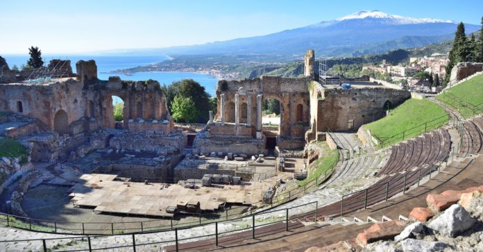 La Sicilia canta Dante - nella foto una veduta aerea del Teatro greco del Palazzolo Acreide, un sito archeologico di un teatro con spalti rotondi orientato verso il mare e sullo sfondo il vulcano