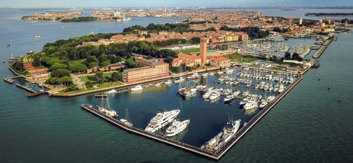 Cinema Santelena una veduta dall'aLTO DI vENEZIA E DELLìISOLA, immersa nella laguna. si vedono delle case antiche di tipica architettura veneziana,, alberi, in primo piano c'è un bellissimo porto con tante barche ancorate