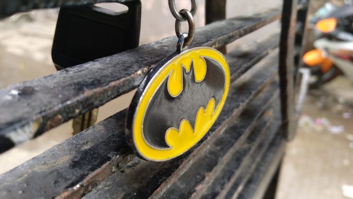 Batman Day - il simbolo di Batman , un pipistrello nero su sfondo giallo, ffatto a pendente, attaccato a una catenella che penzola da una panchina