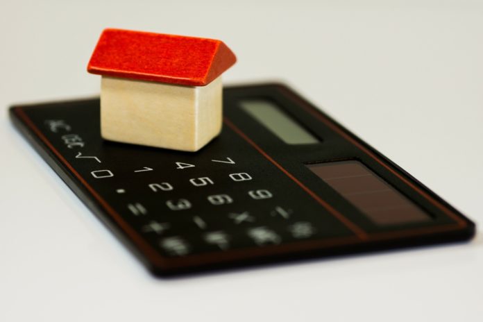 catasto - nella foto una casettina con il tetto rosso e le mura beige è appoggiata su una calcolatrice nera