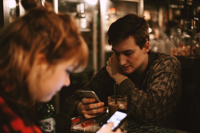 phubbing - una coppia al bar, tutti e due consultano il loro smartphone