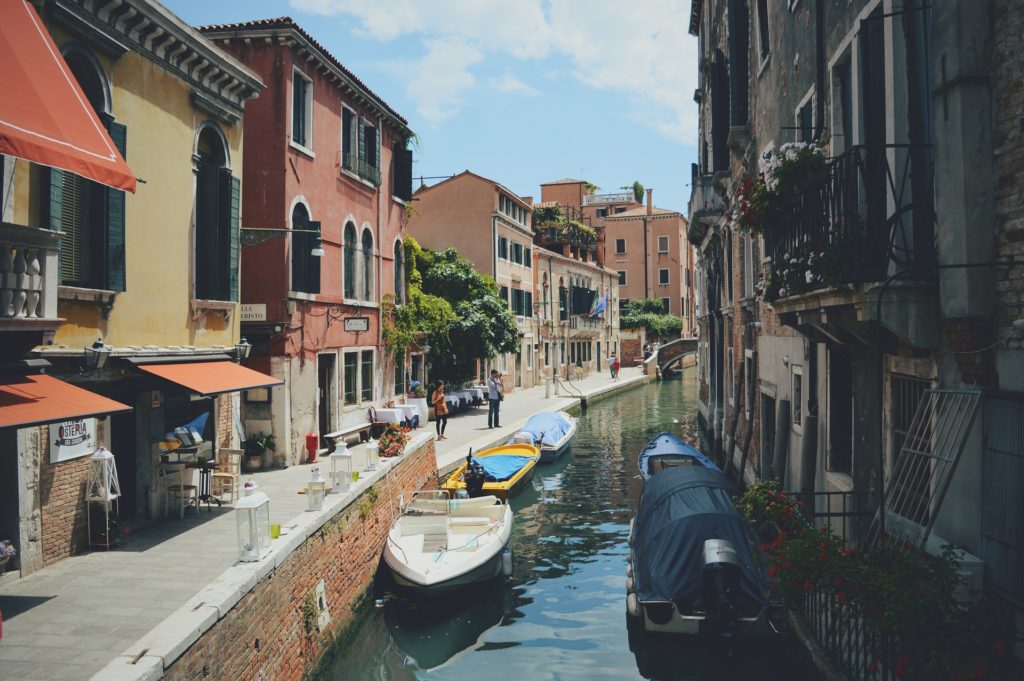 casa e investimenti a Venezia - nella foto dsi vede un canakle con delle barche azzurre e bianche, delle gondole e ai bordi del canale delle case