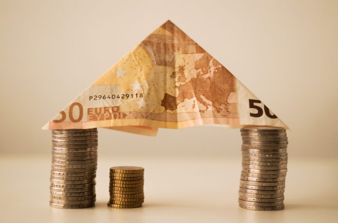 Casa e investimenti - una banconota da 50 euro piegata a triangolo, appoggiata su due pile di monete da un euro, insieme formano la figura di una casa