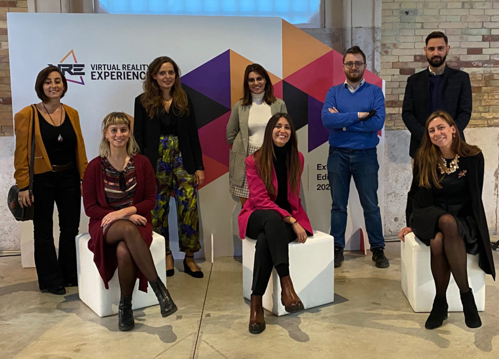 Next Generation to you: lo staff. tre ragazze sedute su dei cubi bianchi, due ragazzi e due ragazze invece stanno in piedi, detro di loro dei pannelli pubblicitari fell'incontroi,