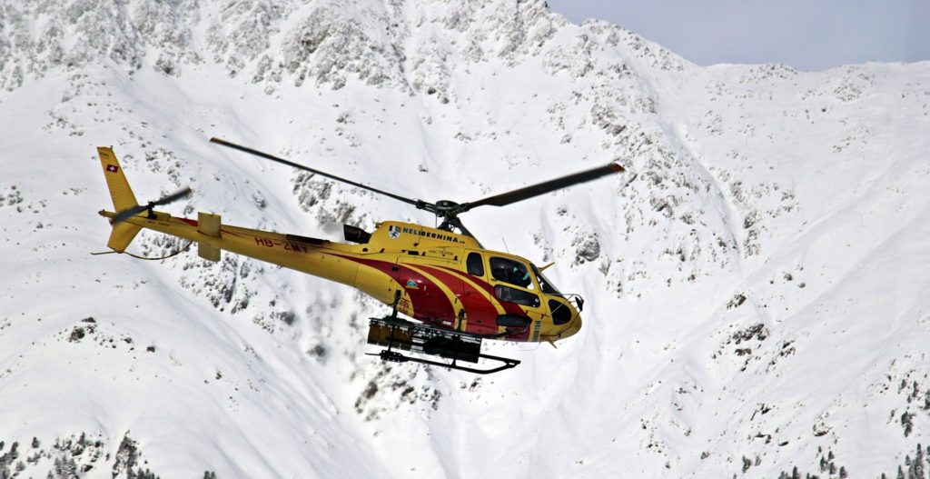 Piste da sci -un elicottero giallo da soccoroso aalpino vola tra le montagne innevate