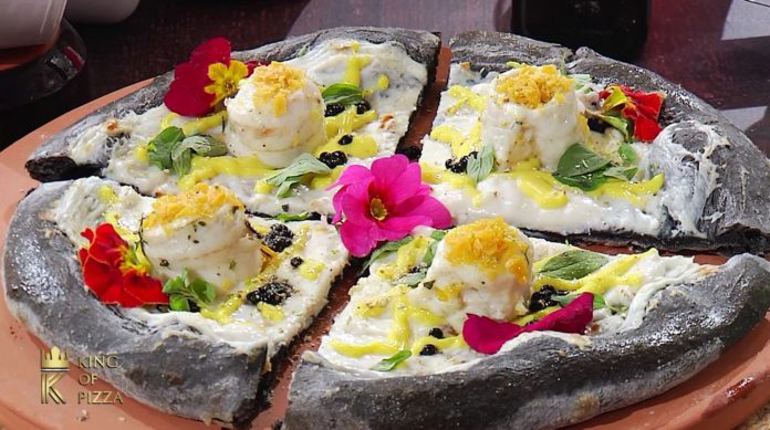 una pizza fatta con farina nera di carbone, con sopra formaggio, e fiori