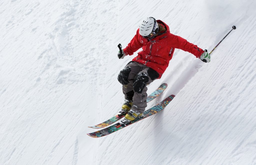 Piste da sci con uno sciatore vestito con una giacca a vento rossa, casco bianco, mentre scende con gli sci