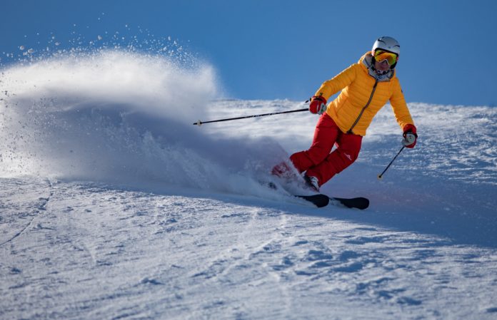 Piste da sci con un o sciatore che scia indossando una giacca a vento gialla e pantaloni rossi, sciando alza una polvere di neve
