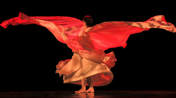Natale in danza - nella foto una ballerina vestita di rossa su sfondo nero. Il suo vestito lungo volteggia aprendosi come ali d'uccello