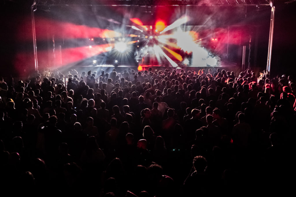 istituto di candiolo - un palco con una band che si sta esibendo, e un pubblico folto sotto il palco . le luci sono rosse