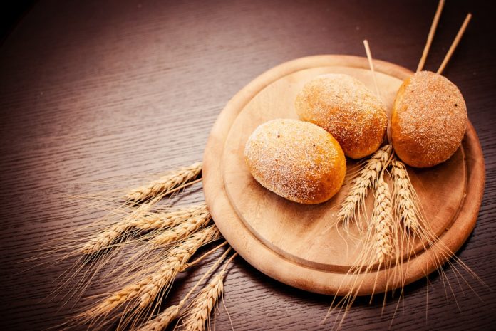 Glutine, celiachia, intolleranza, glutine, sensibilità, alimentazione. Un tagliere in legno con sopra delle pagnotte di pane e delle spighe di grano.