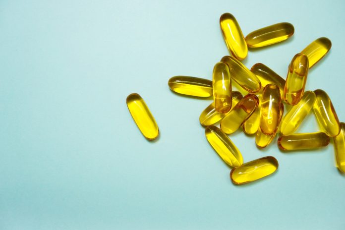 Omega 3, alimentazione, integratori alimentari, proprietà benefiche. Immagine a sfondo azzurro e sulla destra capsule di omega 3 di colore giallo paglierino.