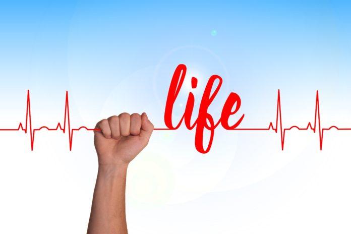 Guarire,emozioni, mondo, amare. una mano che tiene fermo un elettrocardiogramma con la scritta life