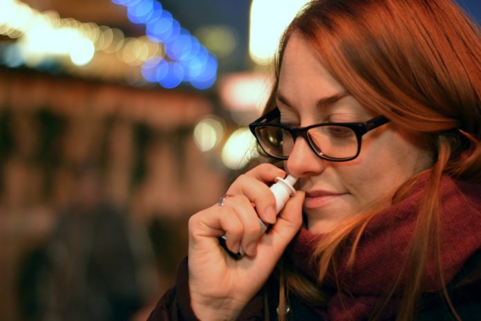 spray nasale anti covid-19 - nella foto una ragazza con capelli rossicci e occhiali neri sta inalando uno spray nasale