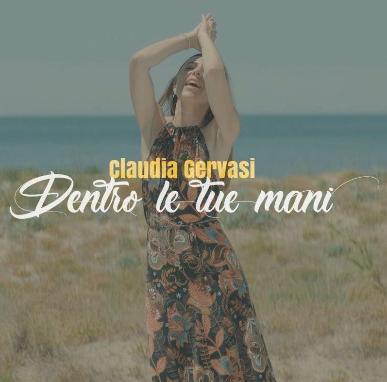 claudia gervasi - la copertina del singolo dentro le tue mani, che la ritrae su una spiaggia, con un vestito etivo a fiori, le mani sopra la testa
