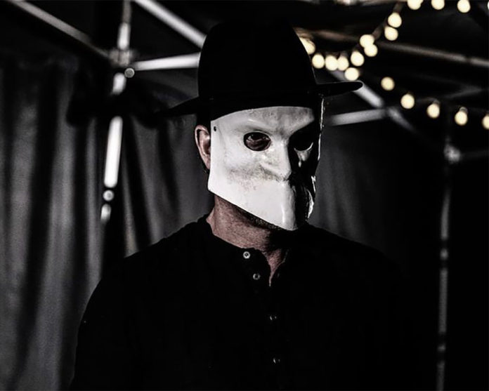 patagonia - pianista indie, vestito di nero, cappello nero in testa, il viso coperto da una maschera bianca