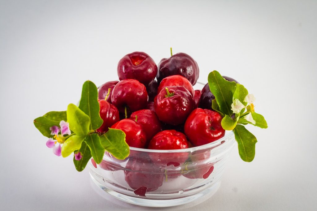 Una ciotolina in vetro in cui all'interno vi sono i frutti dell'acerola. Sono di colore rosso vivo, molto simili ale ciliegie. 