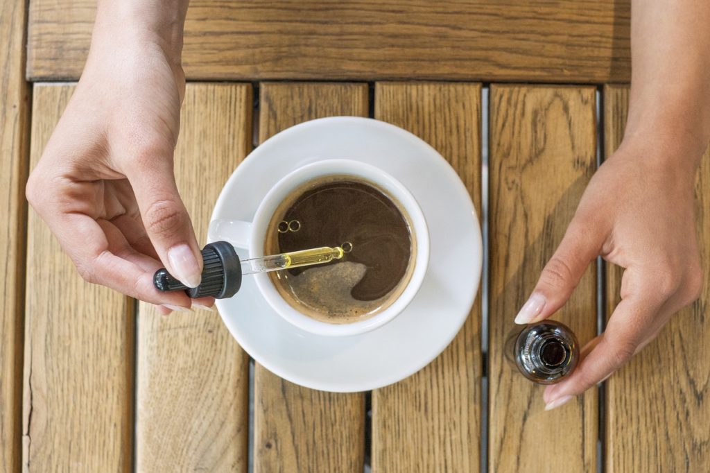 Una ragazza mentre aggiunge qualche goccia di olio di semi di canapa all'interno di una tazza di caffè. 