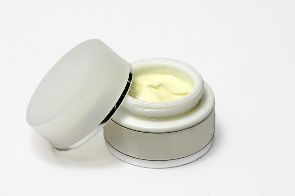 Un barattolino di crema per il viso con all'interno il prodotto cosmetico che possiede un colore giallo chiaro. 
