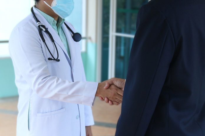 Pregliasco - nella foto un medico con camice bianco, stretoscopio attorno al collo, stringe la mano ad un uomo vosto di schiena, che indossa una giacca scura