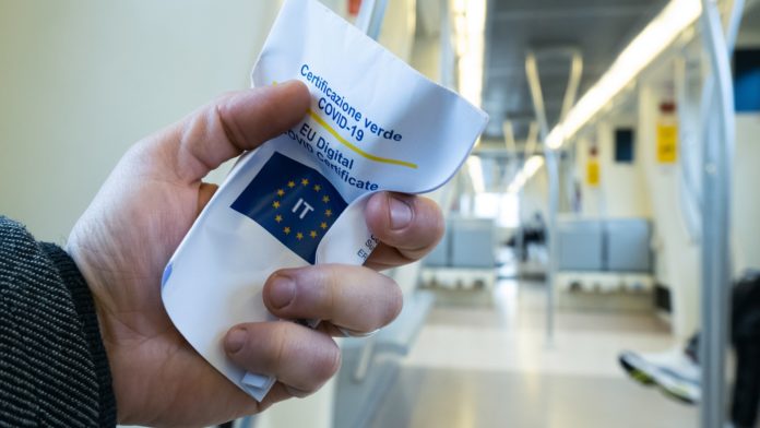 multe anche per vaccinati - nella foto una mano stringe il foglio di una certificazione verde. Si presume che la persona sia in un aeroporto perchè sullo sfondo si vedono sedie di sale d'attesa