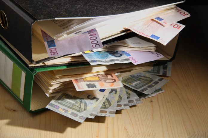 cartelle esattoriali dentro un faldone d'ufficio dal quale fuoriescono diverse banconote di ogni tagli di euro