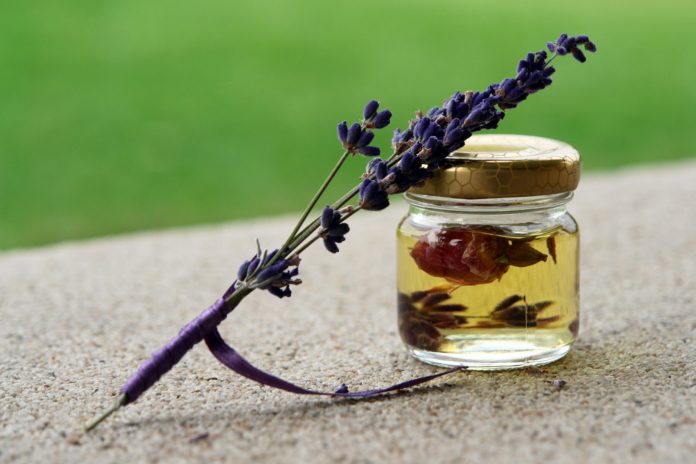 essenze flloreali rinchiuse in un vasetto con dentro dei petali di rosa e sul coperchio del vasetto è appoggiato un rametto di lavanda