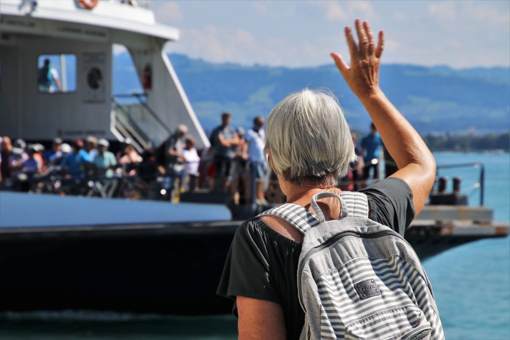 Traghetti da messina - una donna di schiena, con zaino sulle spalle, capelli bianchi, saluta della gente che è affacciata sul ponte di un traghetto