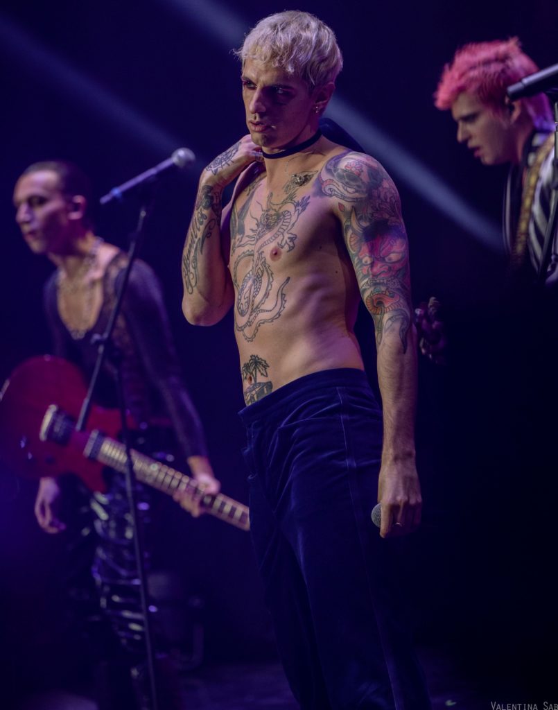 Eurovision Song Contest -  Achille Lauro a petto nudo, con tanti tatuaggi in vista,, indossa un pantalone scuro è in posa con un braccio lungo il fianco e cl'altro piegato sotto il collo, tiene in mano un microfono mentre si esibisce sul palco del concorso "Una voce per San Marino".