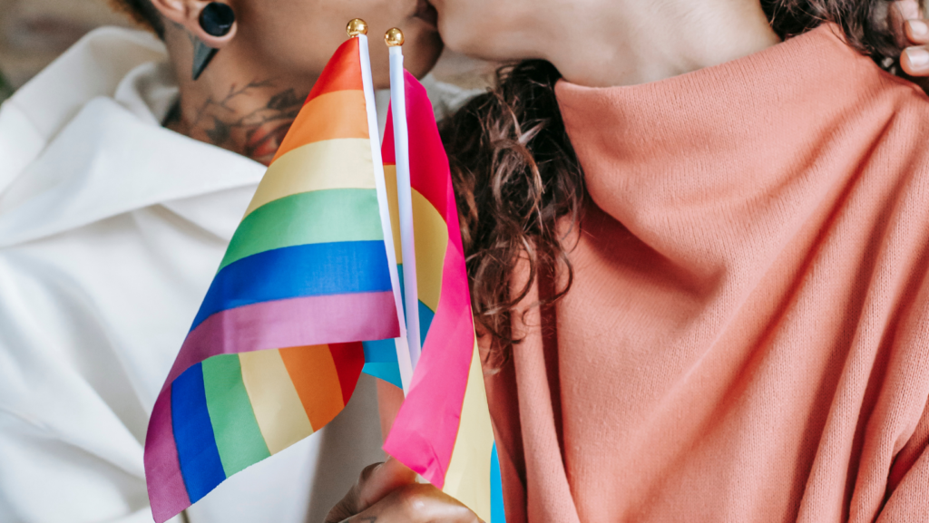 24.000 baci - Due ragazze si scambiano un bacio mentre con le mani intrecciate tengono le bandierine arcobaleno della comunità LGBTQ+. 