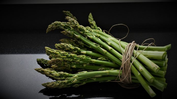 Acido folico, vitamina b9, alimenti, integratori alimentari . Sfondo nero con un mazzo di asparagi di colore verde vivo.