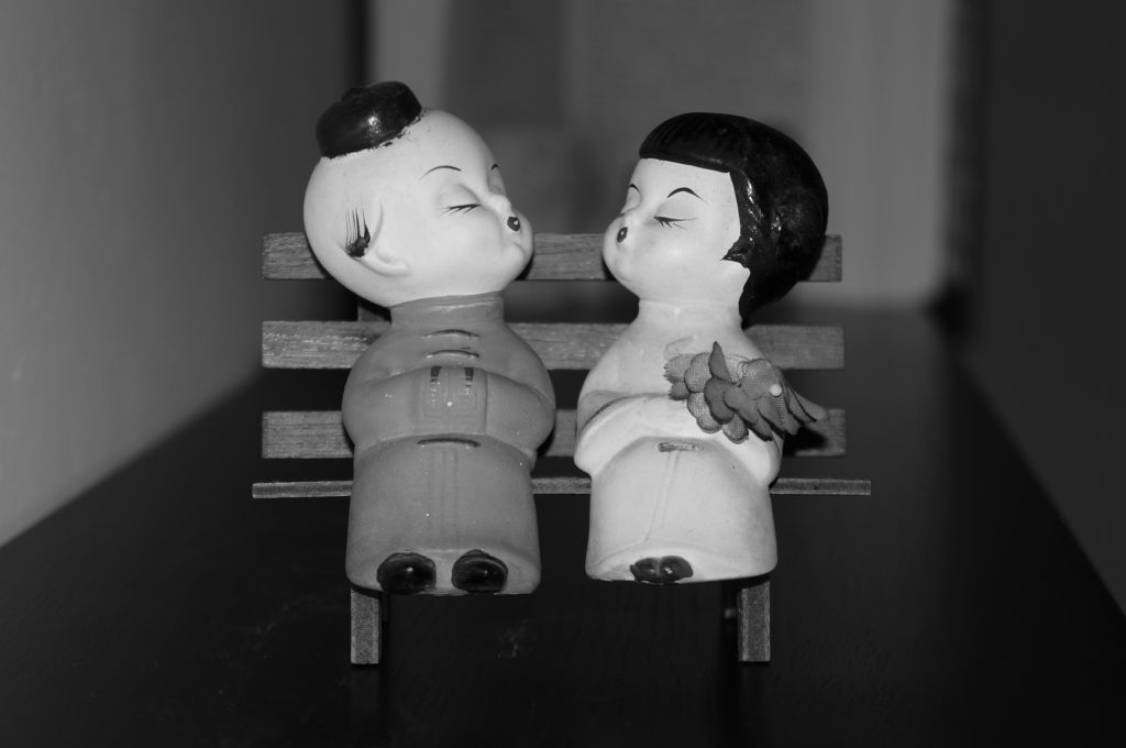 foto in bianco e nero due pupazzetti cinesi seduti su una panchina di legno si mandano un bacio