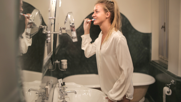 dentifricio e come lavarsi i denti una donna davanti allo specchio in bagno si lava i denti