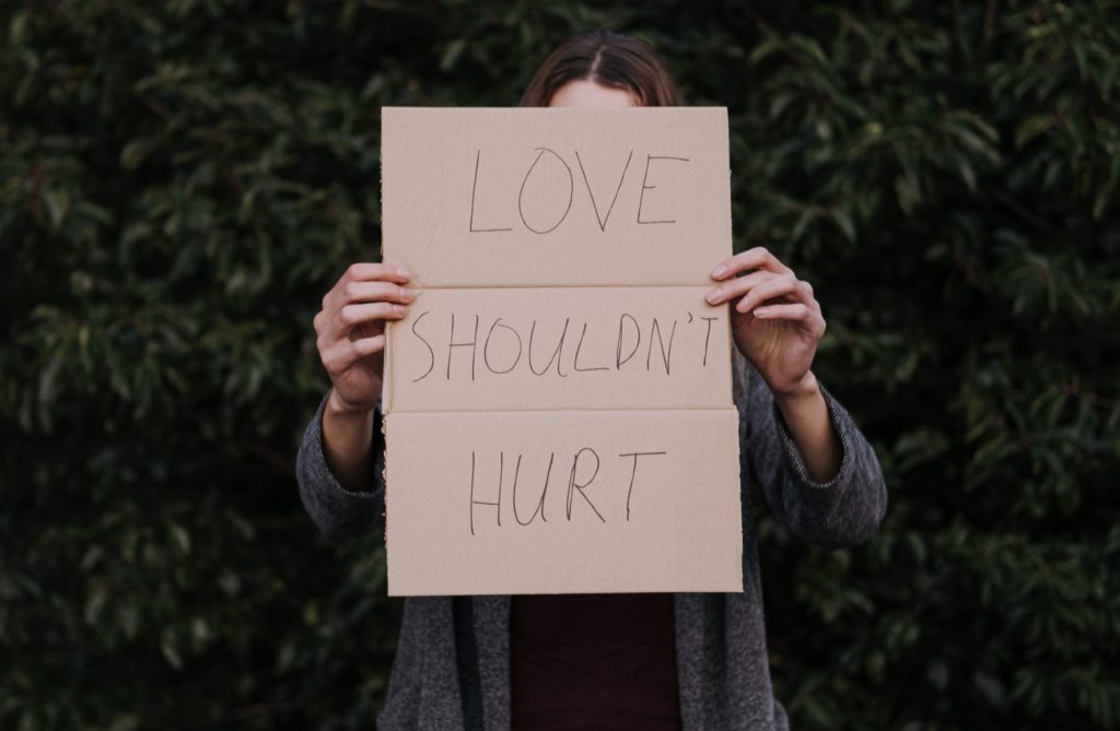 una donna tiene in mano un cartello con su scritto "love shouldn't hurt"
