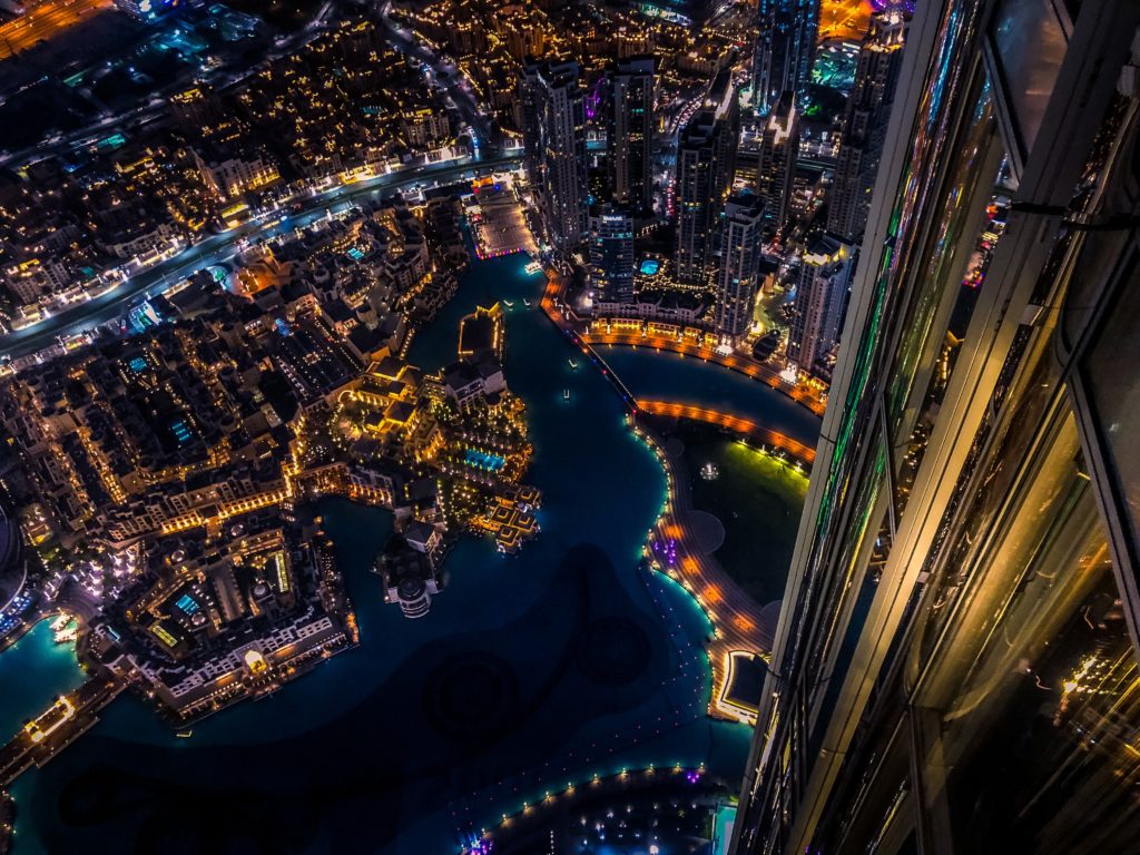 JGT- Vista notturna e dall'alto di parte della città di Dubai. Si vedono grattacieli e strade illuminate da luci colorate.