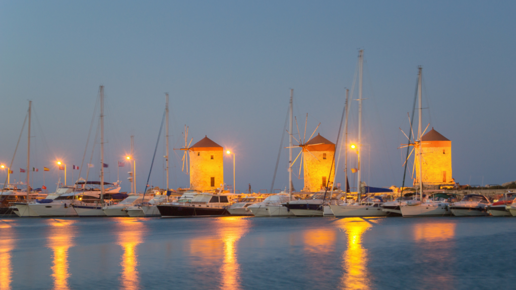 I Mulini a vento di Rodi sul porto con le luci della sera e barche