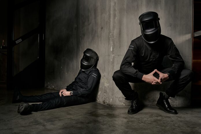 i saldatori vestiti di nero, uno seduto a terra, l'altro piegato sulle ginocchia, indossano entrambi un casco da saldatore