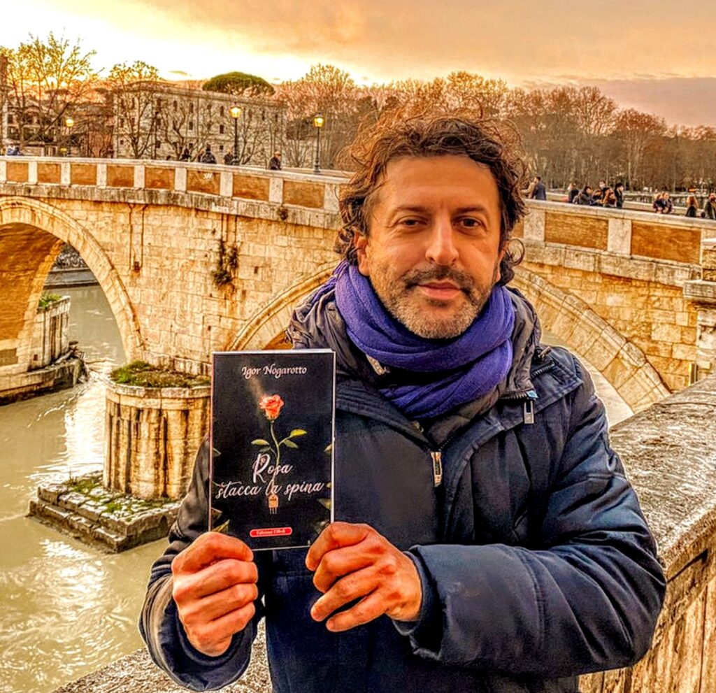 rosa stacca la spina - igor nogarotto che indossa una giacca a vento blu, con il libro tra le mani, sullo sfondo un ponte di roma