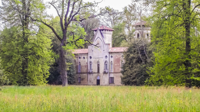CASTELLO MIRADOLO- L'edificio presenta due torri che ricordano un castello medievale. La villa è fotografata dal prato antistante, mentre ai lati dell'edificio ci sono grandi alberi. Il tetto che sovrasta la porta principale è molto alto e spiovente.