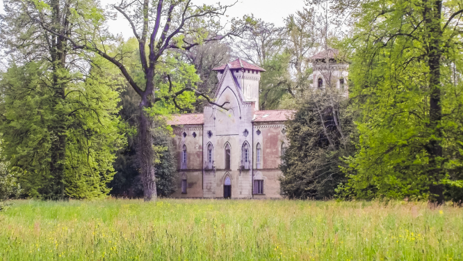 CASTELLO MIRADOLO- L'edificio presenta due torri che ricordano un castello medievale. La villa è fotografata dal prato antistante, mentre ai lati dell'edificio ci sono grandi alberi. Il tetto che sovrasta la porta principale è molto alto e spiovente. 