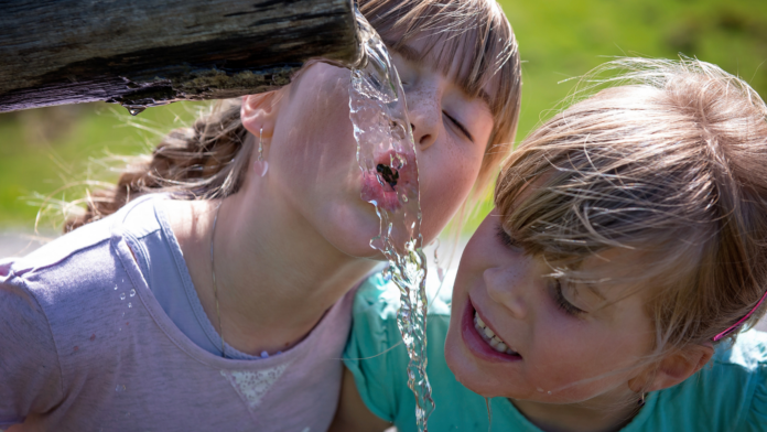 deglutizione atipica o infantile e respirazione orale, due bambii che deglutiscono acqua a una fontana scena estiva
