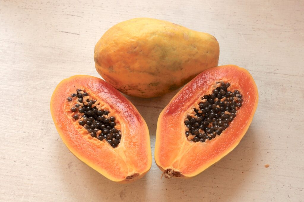 Due frutti di papaya su un tavolo. Uno intero e il secondo tagliato a metà. 