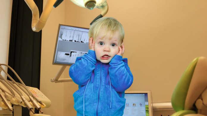 Un bambino piccolo in giacca blu spaventato di fronte alle poltrone del dentista