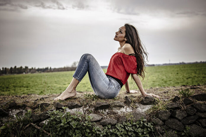 deborah italia seduta su un muretto, a piedi nudi, indossa jeans blu e una maglia scollata rossa