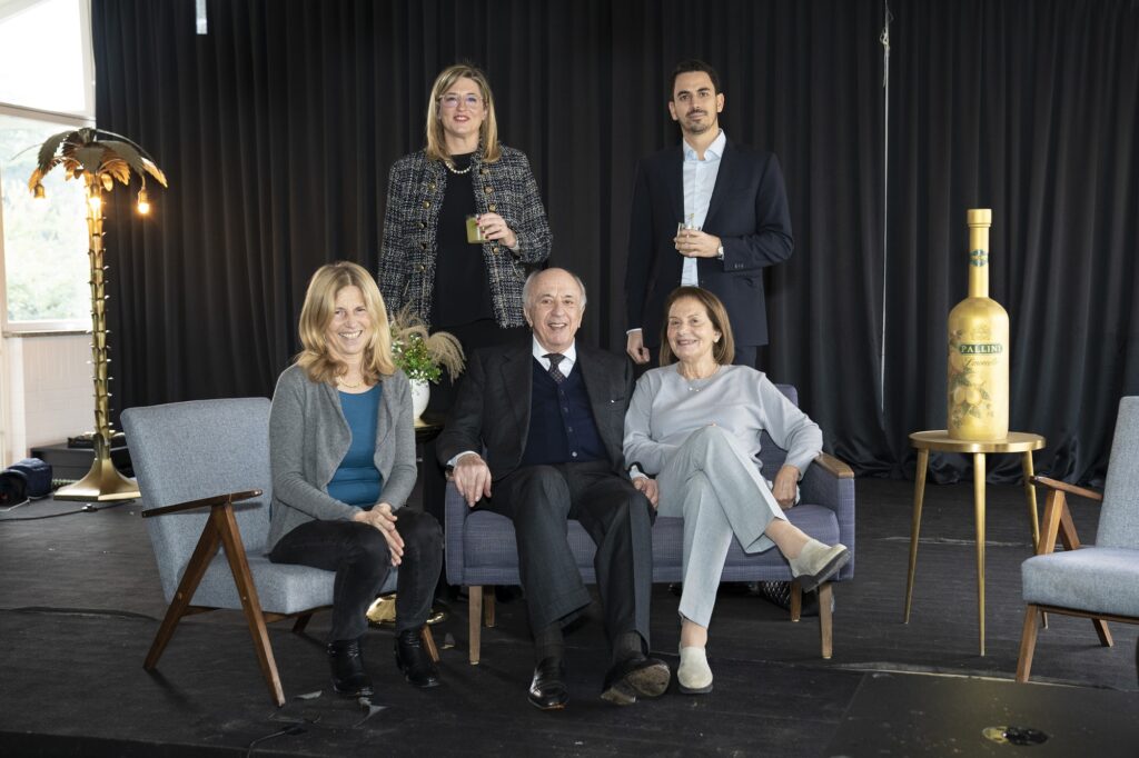 la famiglia Pallini, in un afoto di rito. TRe donne  due uomini vestiti eleganti, 3 seduti su un divanetto e due in piedi dietro di loro. Affianco, sulla destra, un tavolino con sopra una bottiglia dorata di limoncello