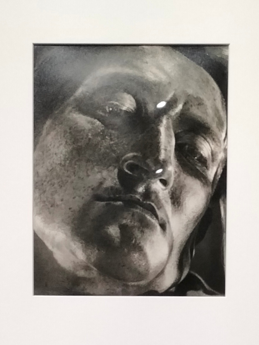 MOMA- foto in bianco e nero di un volto. Il fotografo lo riprende dal basso, la luce illumina il viso da sinistra e l'espressione sembra sofferente. 