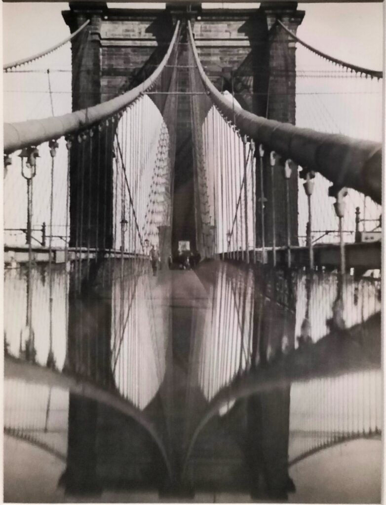 CAMERA- Foto in bianco e nero del ponte di Brooklyn. La struttura si fonde con il suo riflesso creato nelle pozzanghere.  
